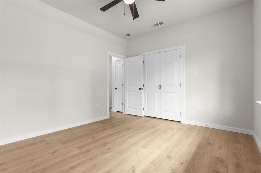 Spacious interior room featuring wood-finish flooring, white walls, and a ceiling fan