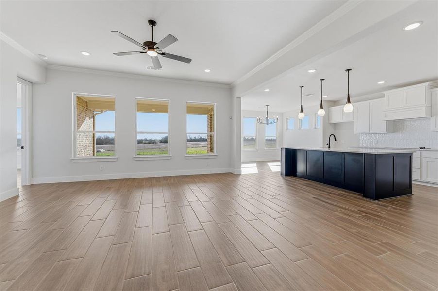 Unfurnished living room with ornamental molding, wood finish floors, a chandelier, a ceiling fan, and recessed lighting