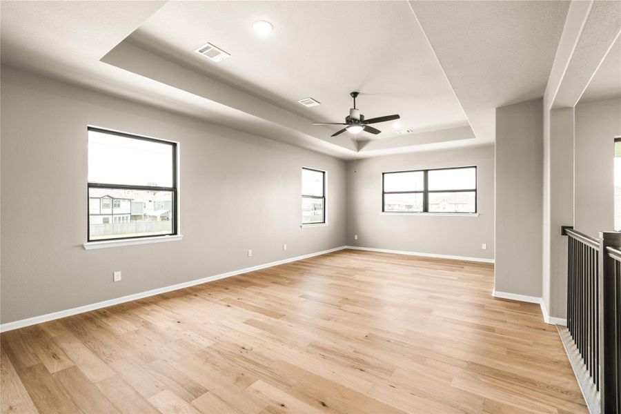 Spacious and bright loft /gameroom area with elegant wood flooring, a modern ceiling fan, high ceiling, and a plethora of windows that invite natural light.