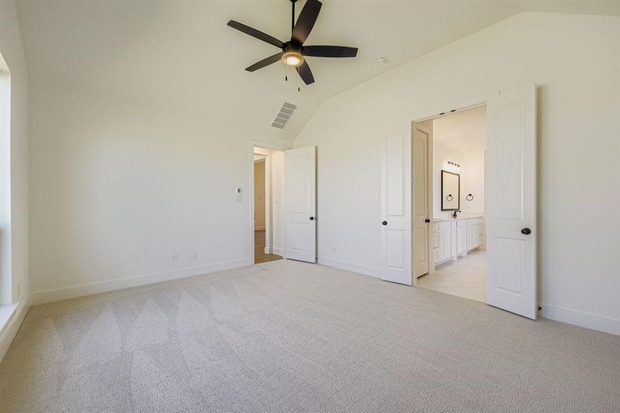 Unfurnished bedroom with light colored carpet, lofted ceiling, ceiling fan, and ensuite bathroom Unfurnished bedroom with light colored carpet, lofted ceiling, ceiling fan, and ensuite bathroom