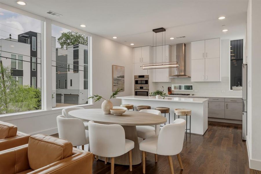 This open-concept living space features hardwood floors, large windows providing ample natural light, and a modern kitchen with a large island and stainless steel appliances