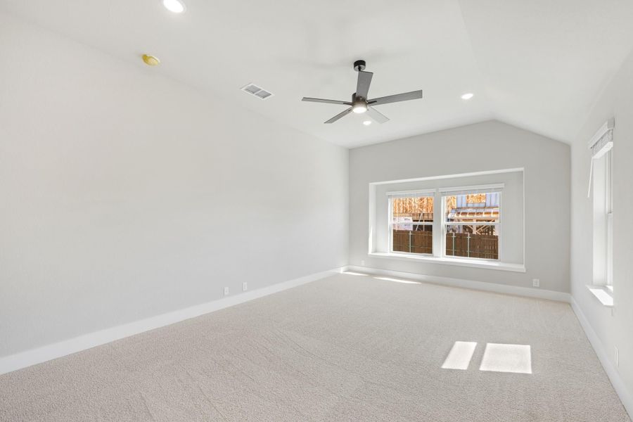 Empty bedroom with vaulted ceiling, ceiling fan, carpet flooring, and a large window