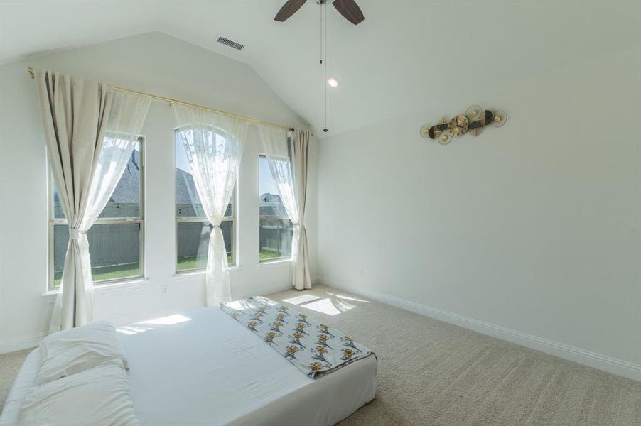 Vaulted ceiling room featuring three large windows, light neutral wall paint, and beige carpeting