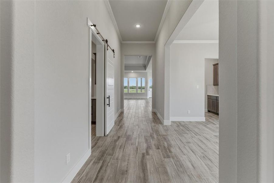 Expansive hallway featuring wood-finish flooring, a contemporary barn door with black hardware, recessed ceiling lighting, crown molding, and a wide entryway
