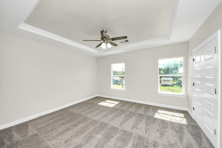 Step into the stunning primary suite, a spacious retreat designed for both comfort and style, offering plenty of room for all your favorite bedroom furniture. Flooded with natural light from large windows, this serene space is elevated by elegant crown molding, a sophisticated tray ceiling, and a stylish ceiling fan - (representation photo).