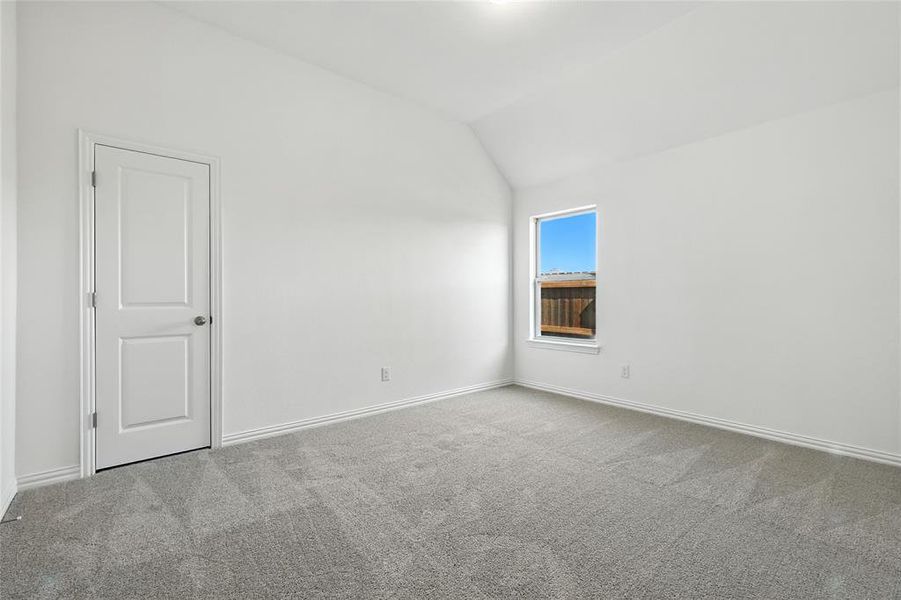 Carpeted spare room featuring vaulted ceiling and baseboards