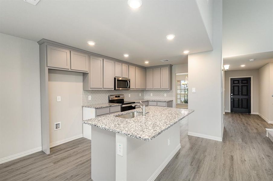 Kitchen featuring light stone counters, stainless steel appliances, sink, a center island with sink, and light hardwood / wood-style floors