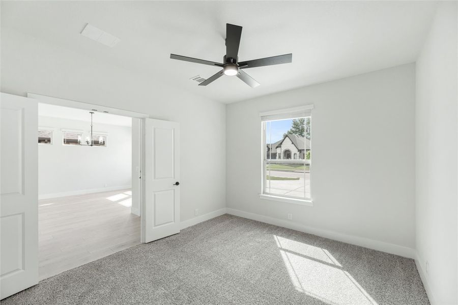 Empty bedroom with gray carpet, black ceiling fan, and open door leading to adjacent room
