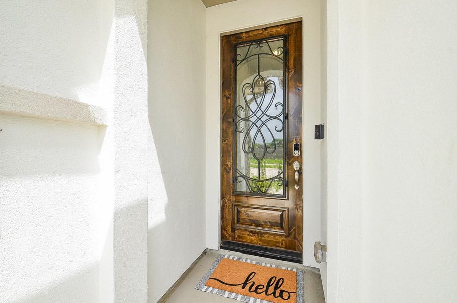 This inviting entry features a stylish wooden door with intricate wrought iron design set against a clean, white stucco exterior.