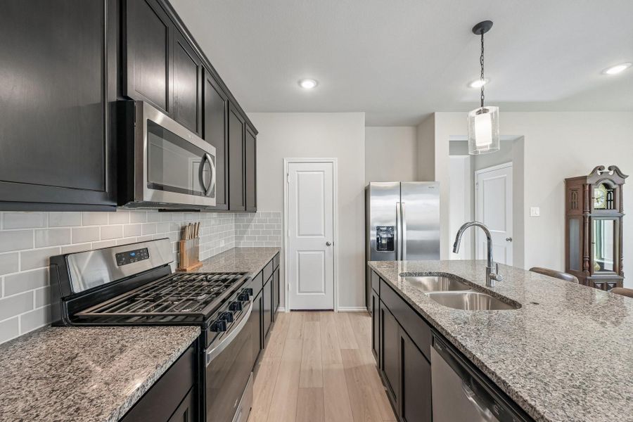 Modern kitchen with sleek dark cabinetry, stainless steel appliances, and a spacious granite-topped island, perfect for culinary enthusiasts.