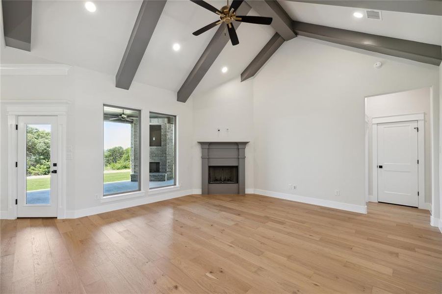 Unfurnished living room with high vaulted ceiling, ceiling fan, light hardwood / wood-style floors, and beam ceiling