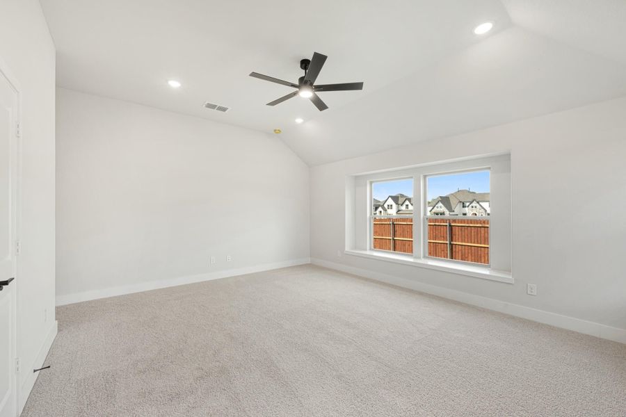 Empty bedroom with vaulted ceiling, ceiling fan, carpet flooring, and large window overlooking neighborhood