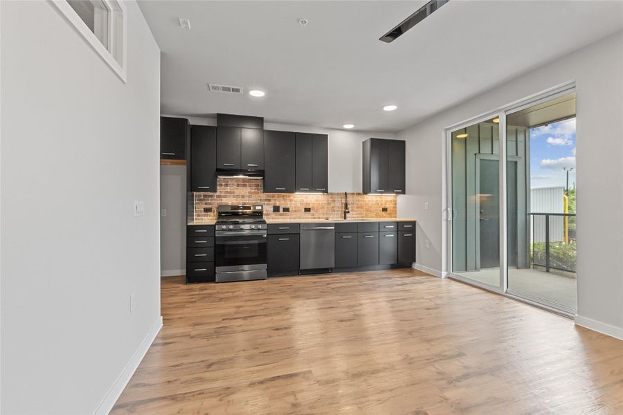 Kitchen featuring appliances with stainless steel finishes, dark cabinets, light countertops, backsplash, and light wood-style flooring