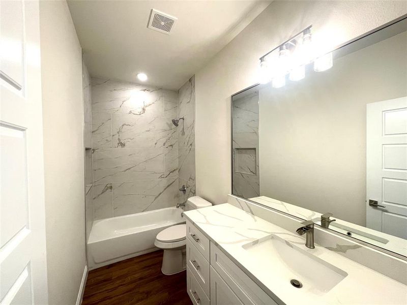 Full bathroom with hardwood / wood-style flooring, vanity, tiled shower / bath combo, and toilet