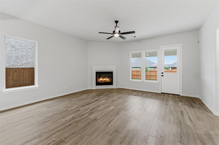 Spacious living area featuring light wood-finish flooring, a contemporary fireplace with a white mantel, and a black ceiling fan