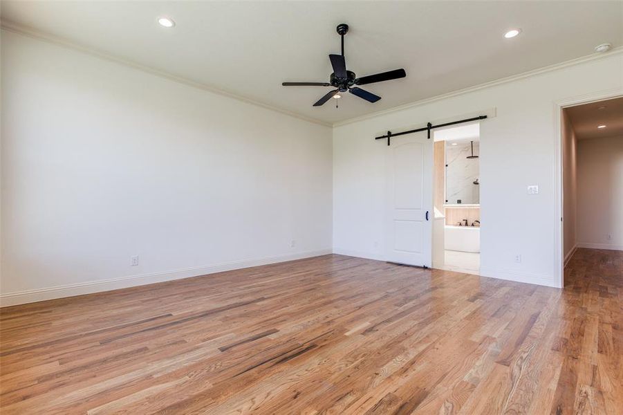 Unfurnished bedroom featuring a barn door, ornamental molding, light wood-type flooring, and ceiling fan