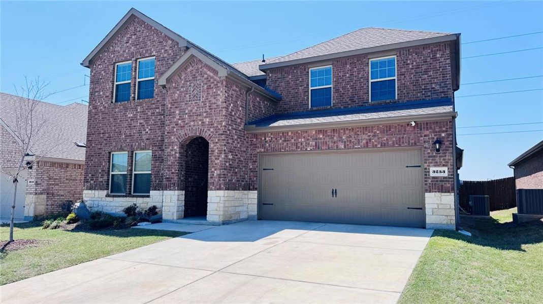 Traditional-style home featuring a front yard, a garage, concrete driveway, central air condition unit, and brick siding