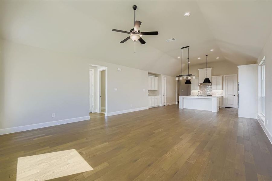 Unfurnished living room with lofted ceiling, light wood-style flooring, recessed lighting, and a ceiling fan Unfurnished living room with lofted ceiling, light wood-style flooring, recessed lighting, and a ceiling fan