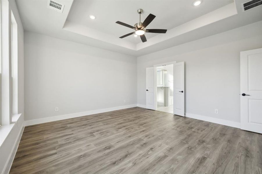 Unfurnished bedroom featuring wood-type flooring, connected bathroom, a tray ceiling, and ceiling fan