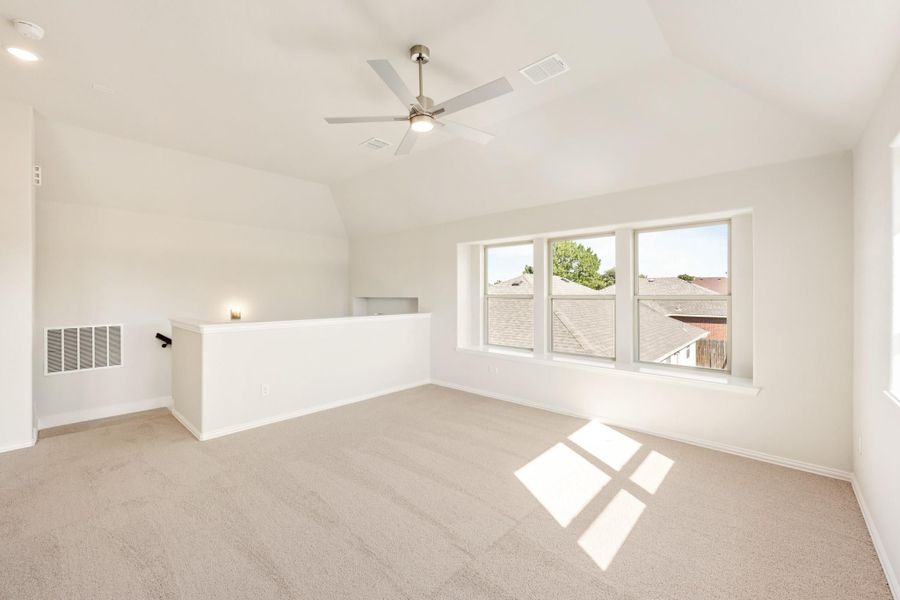 Open upstairs bonus room with vaulted ceiling, ceiling fan, carpet flooring, and large windows overlooking neighboring rooftops Open upstairs bonus room with vaulted ceiling, ceiling fan, carpet flooring, and large windows overlooking neighboring rooftops