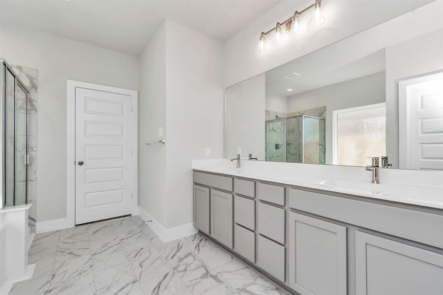 Sophisticated vanity, featuring double sinks, light-colored countertops, contemporary hardware, and exquisite vanity lights. Sample photo of completed home. Actual colors and selections may vary.