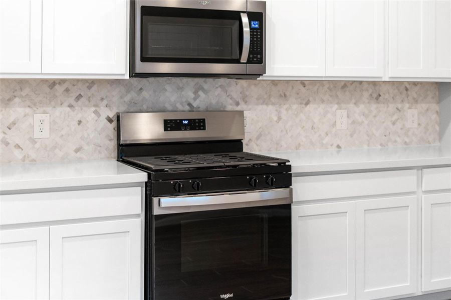 Showcased here is a Whirlpool gas range featuring a versatile center oval burner, paired with a steam microwave equipped with sensor cooking—all framed by the elegant tile backsplash.