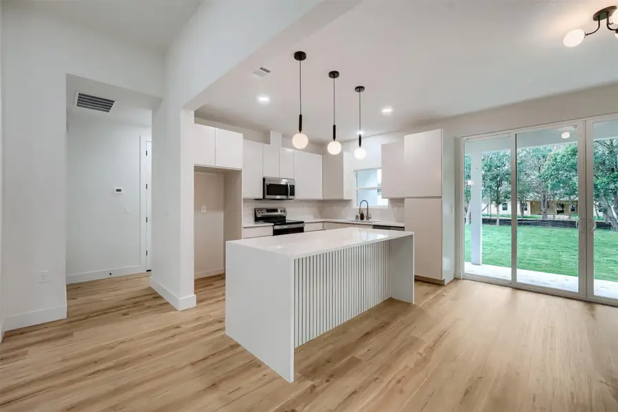 Open-concept kitchen featuring white flat-panel cabinetry, a waterfall island with fluted detailing, and stainless steel appliances