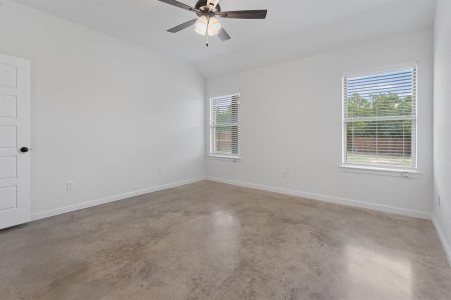 Spare room with vaulted ceiling, concrete floors, and ceiling fan