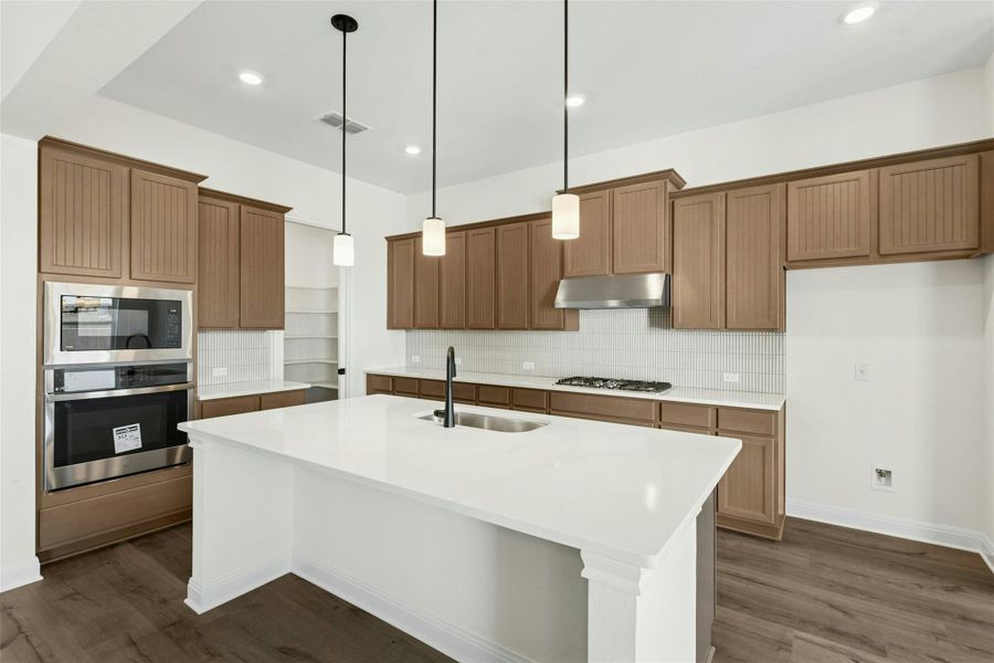 Kitchen with pendant lighting, decorative backsplash, wood finish cabinets, and a center island with sink