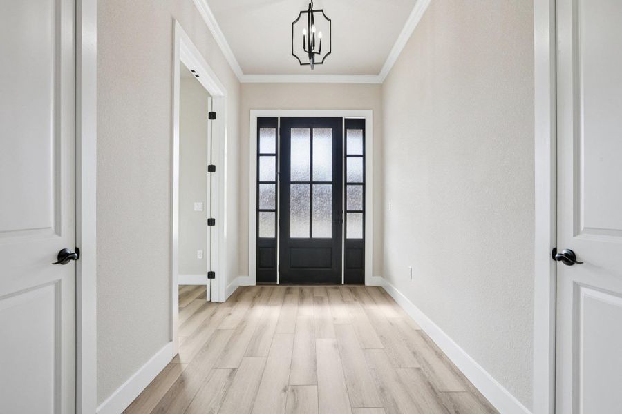 Entryway with ornamental molding, light wood finished floors, and a chandelier