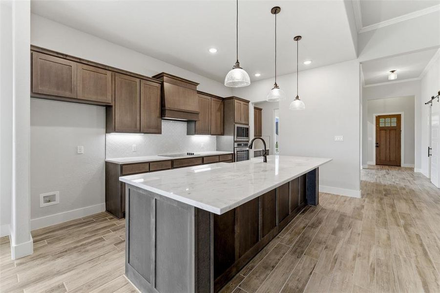 Spacious kitchen featuring a large central island with a light-toned countertop, dark wood-finish cabinetry, and contemporary pendant lighting