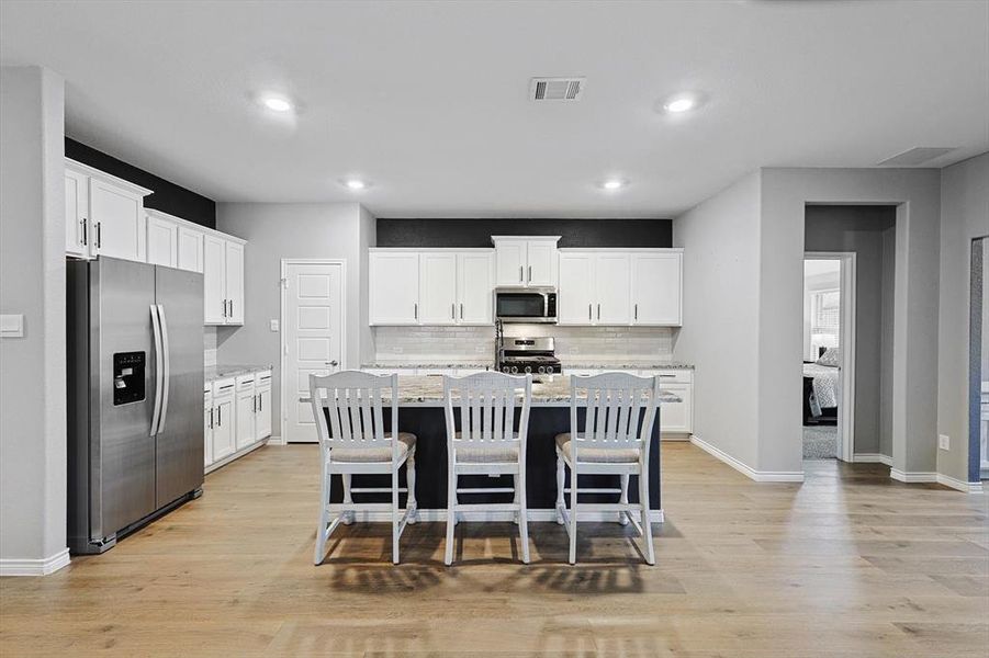 Kitchen with appliances with stainless steel finishes, an island with sink, and white cabinets