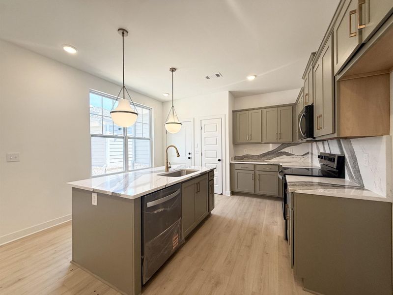 Kitchen featuring light stone countertops, stainless steel appliances, a kitchen island with sink, gray cabinetry, and light wood-style floors