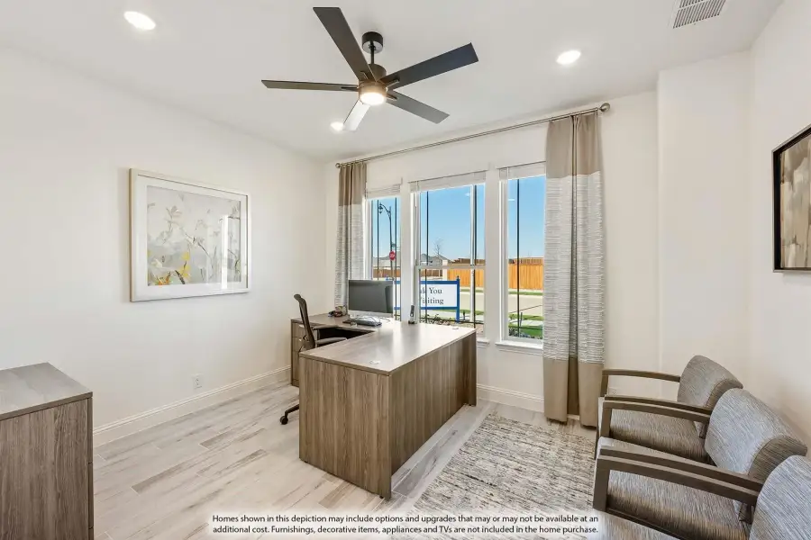 Home office with wood desk, ceiling fan, light hardwood floors, and large windows with neutral drapes