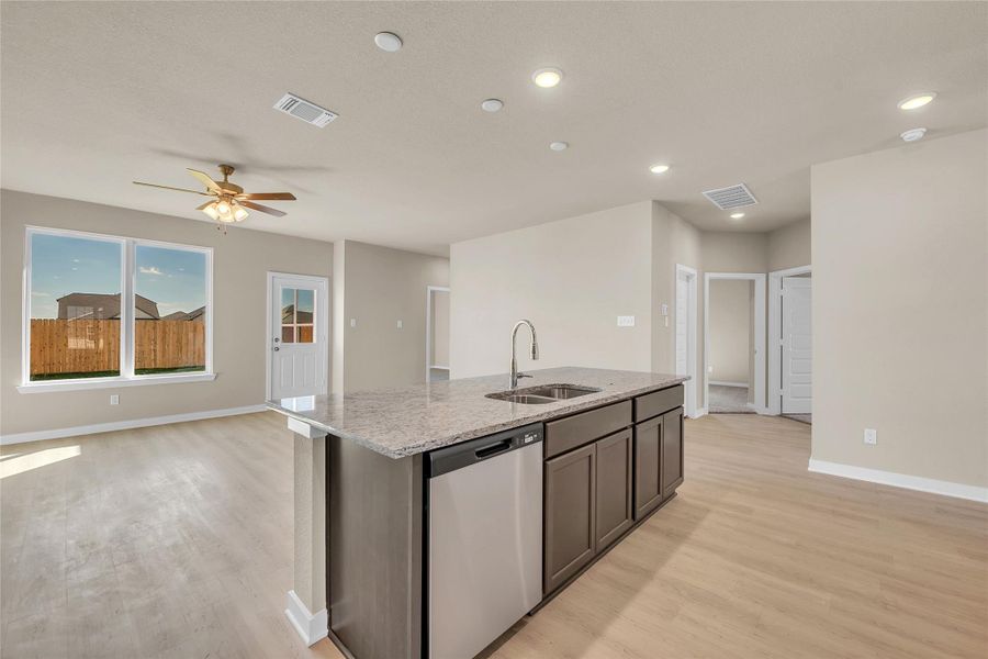 Kitchen featuring dishwasher, light stone counters, light wood-style floors, open floor plan, and a kitchen island with sink