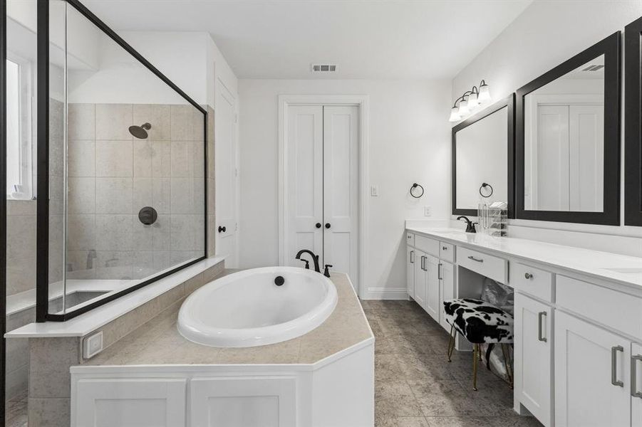 Spacious bathroom featuring a built-in soaking tub, walk-in shower with clear glass enclosure, dual vanity with white countertops, and wood-finish flooring