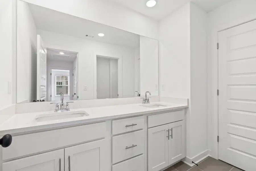 Spacious bathroom vanity featuring dual undermount sinks, quartz countertops, white cabinetry, and a full-width wall mirror