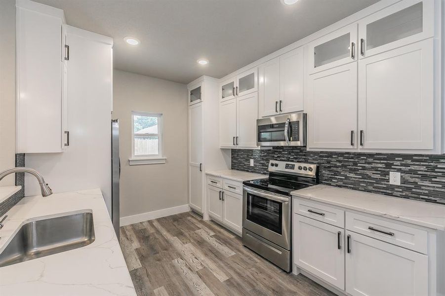 Kitchen with hardwood / wood-style floors, light stone counters, sink, white cabinets, and appliances with stainless steel finishes