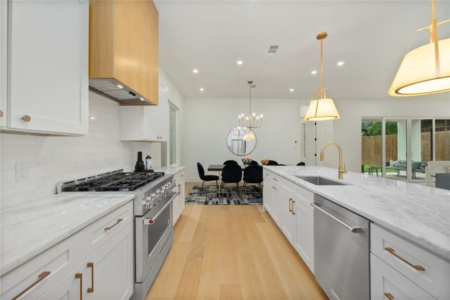 The kitchen features white cabinetry, marble countertops, stainless steel appliances, and light wood flooring