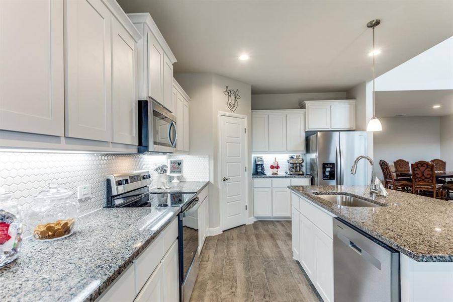 Kitchen with pendant lighting, sink, white cabinets, stainless steel appliances, and light wood-type flooring