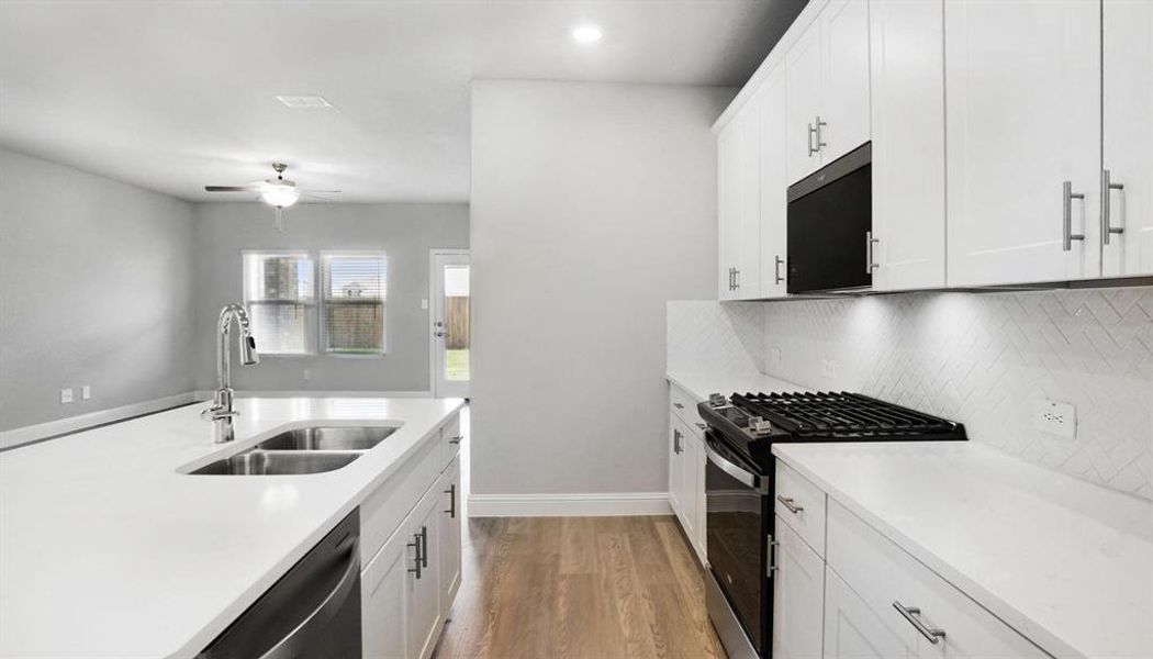 Kitchen with appliances with stainless steel finishes, white cabinetry, light wood finished floors, ceiling fan, and light stone countertops