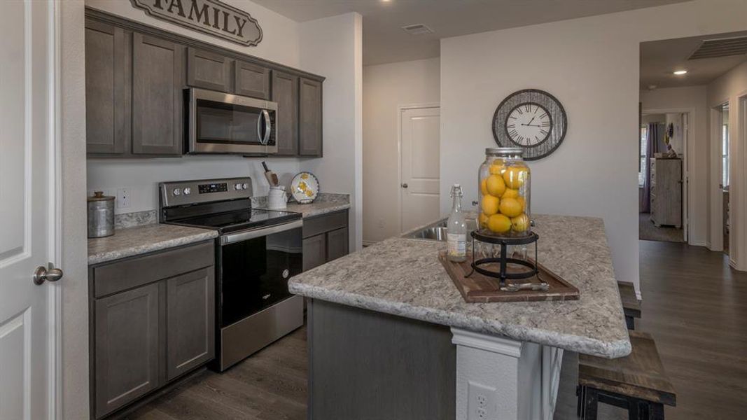 Kitchen with stainless steel appliances, a center island with sink, dark wood-style flooring, dark wood finish cabinets, and a kitchen bar
