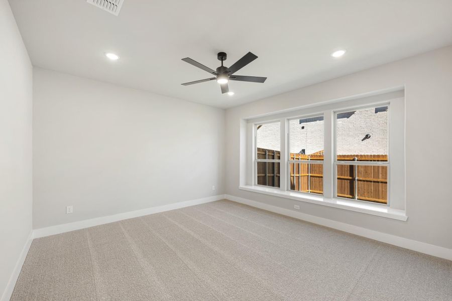 Empty bedroom with carpet flooring, ceiling fan, and triple window overlooking backyard fence