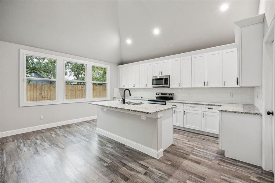 Kitchen with a center island with sink, granite countertop, white cabinetry, tasteful backsplash, and stainless steel appliances