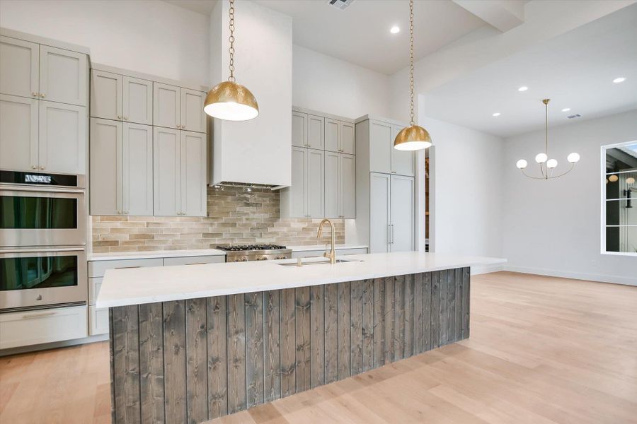 Contemporary kitchen featuring a large central island with a wood-paneled base, light-toned countertop, and brass pendant lighting