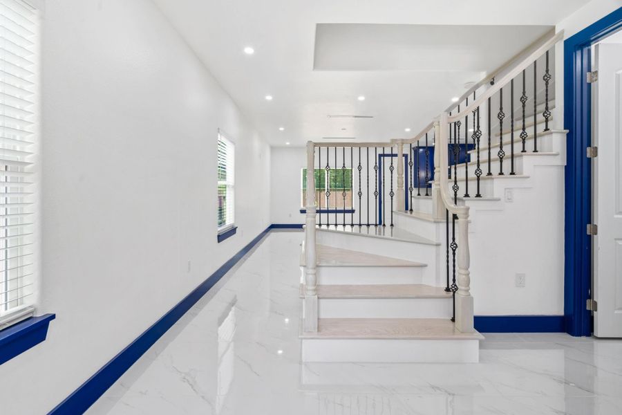 Step right into this stunning interior highlighting a bright, modern design with glossy white floors and striking iron-railed stairs. Blue-accented trim and window sills add a sophisticated pop of color, while large windows flood the space with natural light, creating an open and airy ambiance. Step right into this stunning interior highlighting a bright, modern design with glossy white floors and striking iron-railed stairs. Blue-accented trim and window sills add a sophisticated pop of color, while large windows flood the space with natural light, creating an open and airy ambiance.