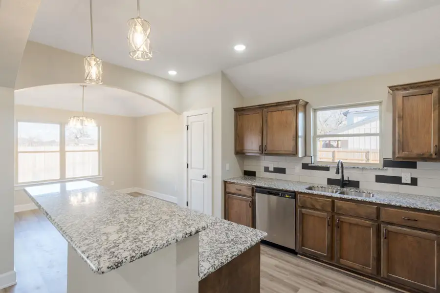 Kitchen featuring light wood-style flooring, a center island, decorative backsplash, dishwasher, and light stone countertops