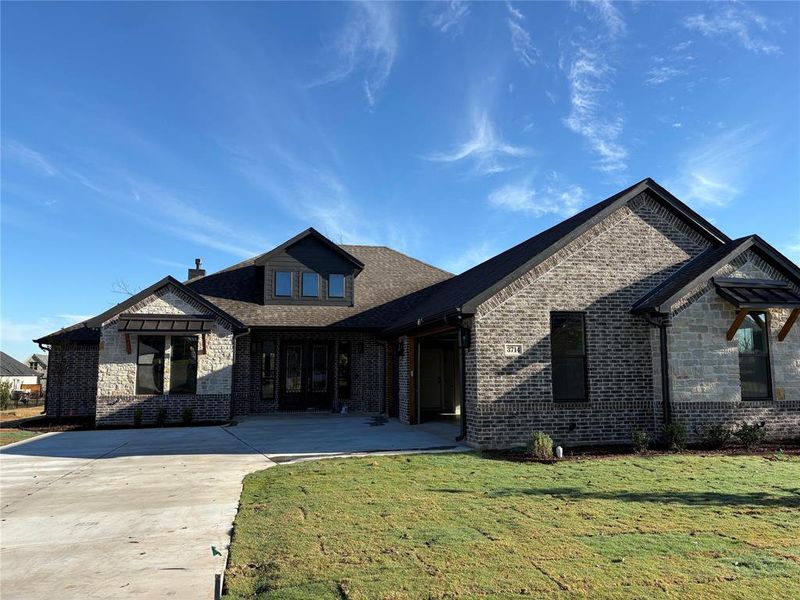 View of front of house featuring brick siding, a front lawn, driveway, and roof with shingles