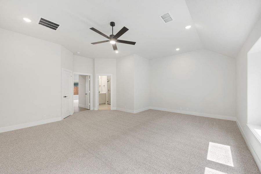 Spacious bedroom with vaulted ceiling, ceiling fan, carpet flooring, and open door to ensuite bathroom