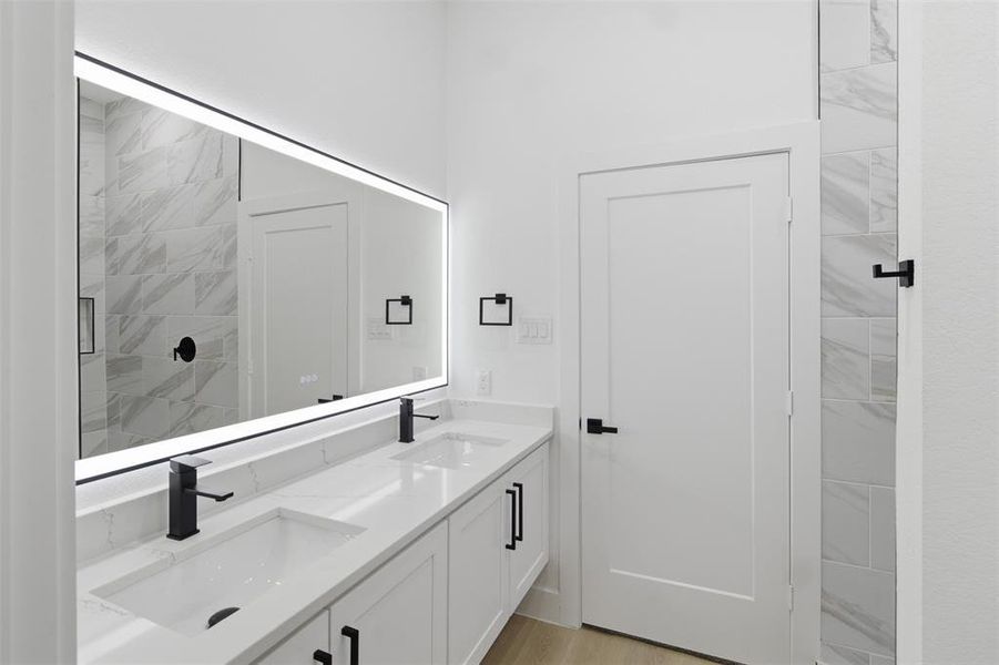 Full bathroom with double vanity, a shower stall, and light wood-style floors